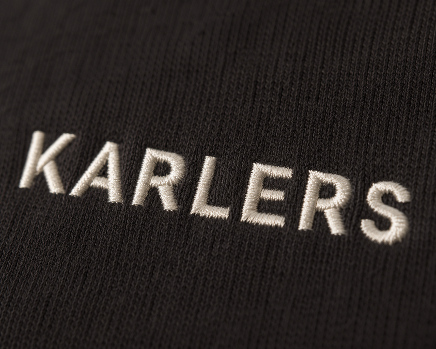 Close-up of bone satin-stitch KARLERS embroidery on near-black cotton fleece
