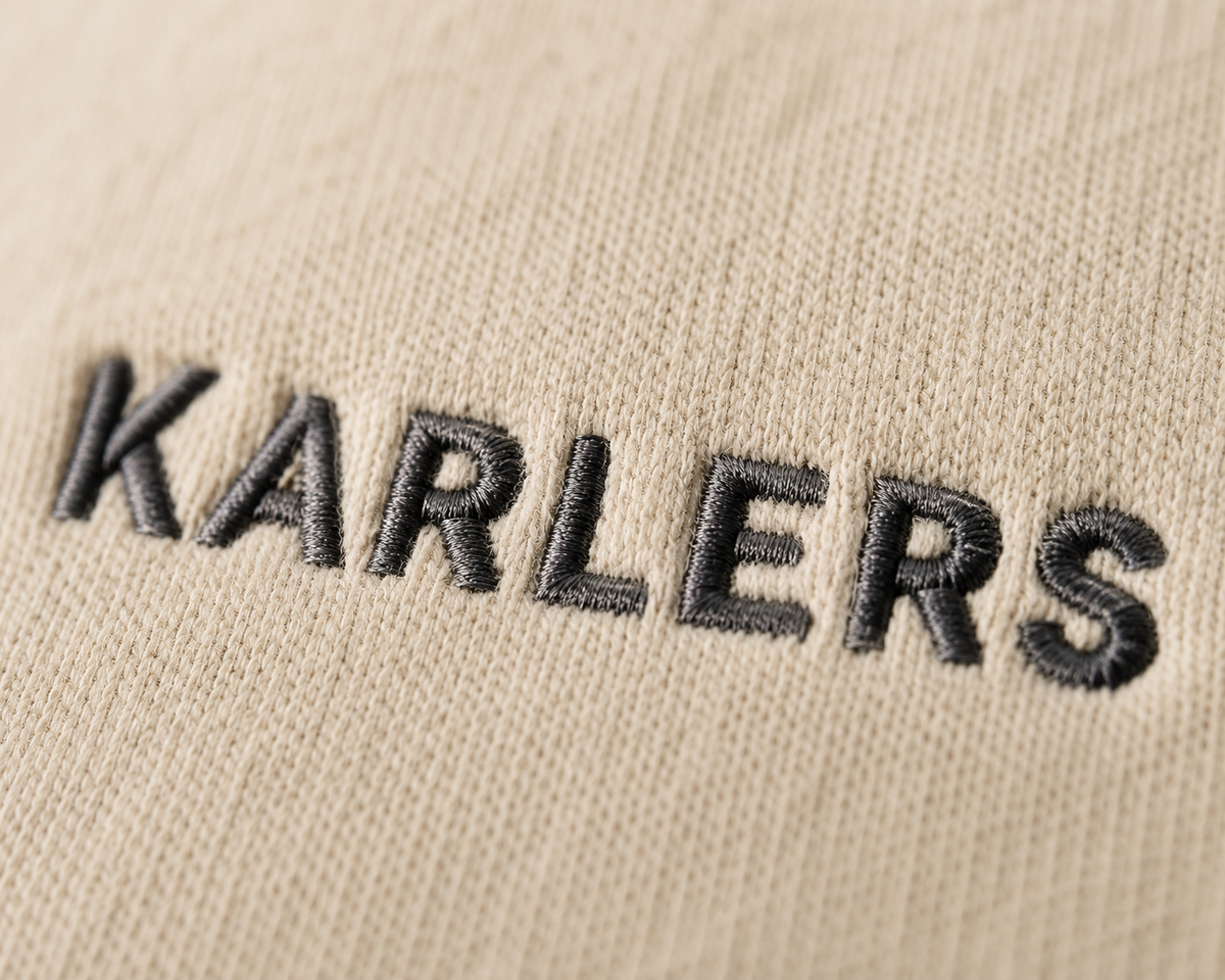 Close-up of the dark grey embroidered KARLERS wordmark on oat cotton fleece