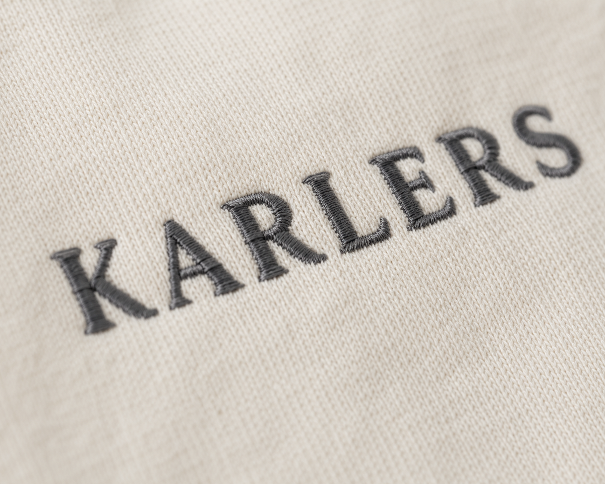 Close-up of the embroidered KARLERS wordmark on bone cotton jersey